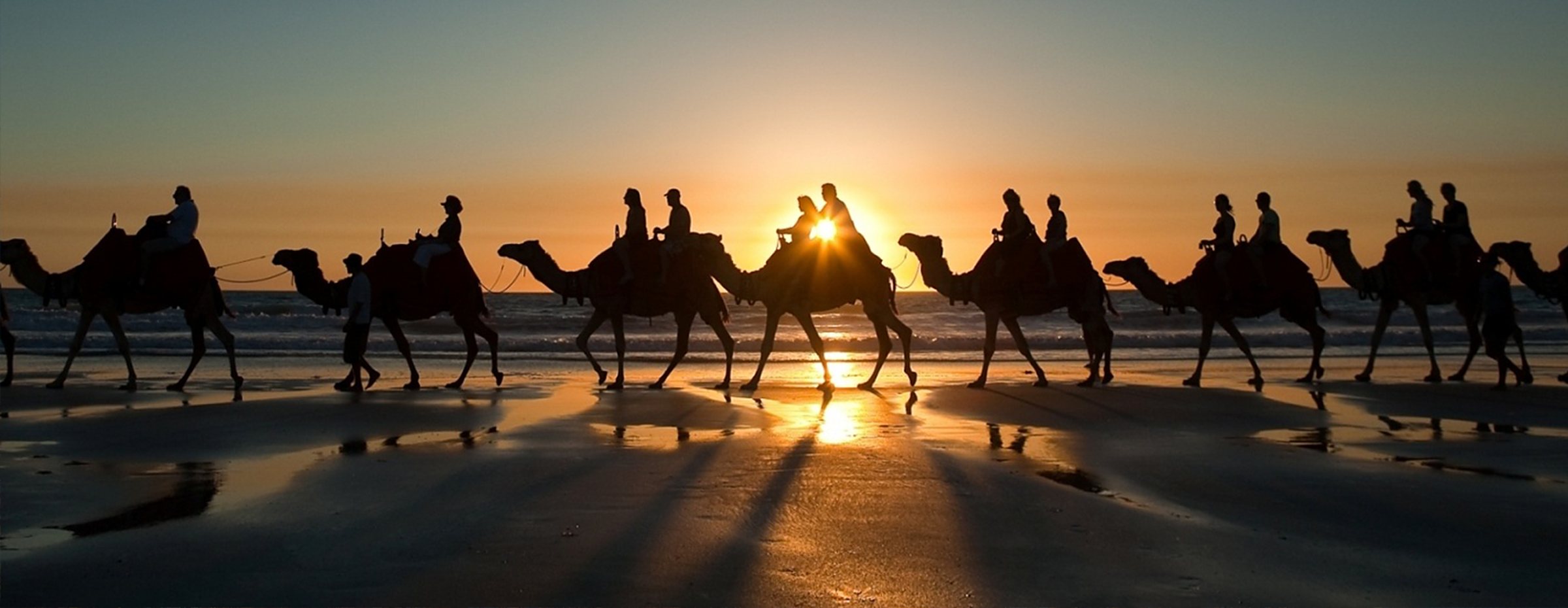 A camel caravan crossing the sand at sunset